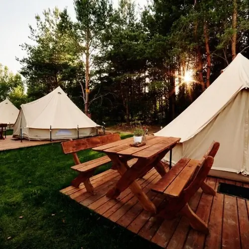 Część jadalniana z drewnianym stołem i ławkami przed namiotem