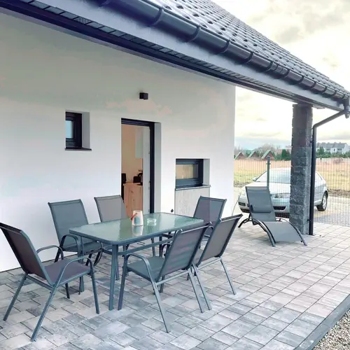 Taras z tyłu domu, zadaszony, z stołem i krzesłami, oddzielony od sąsiedniej części.